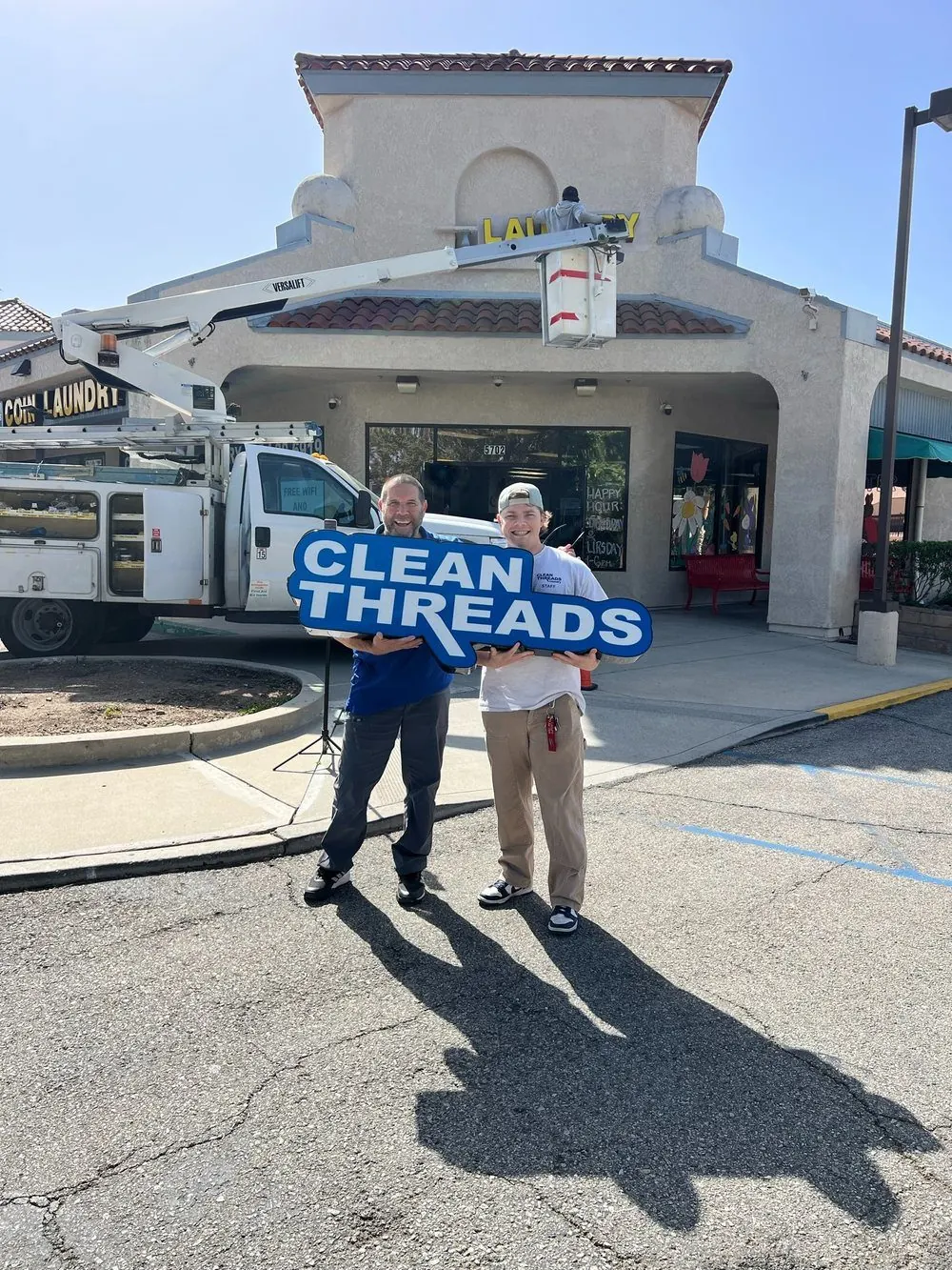 Howard and his son holding the Clean Threads sign outside the laundromat